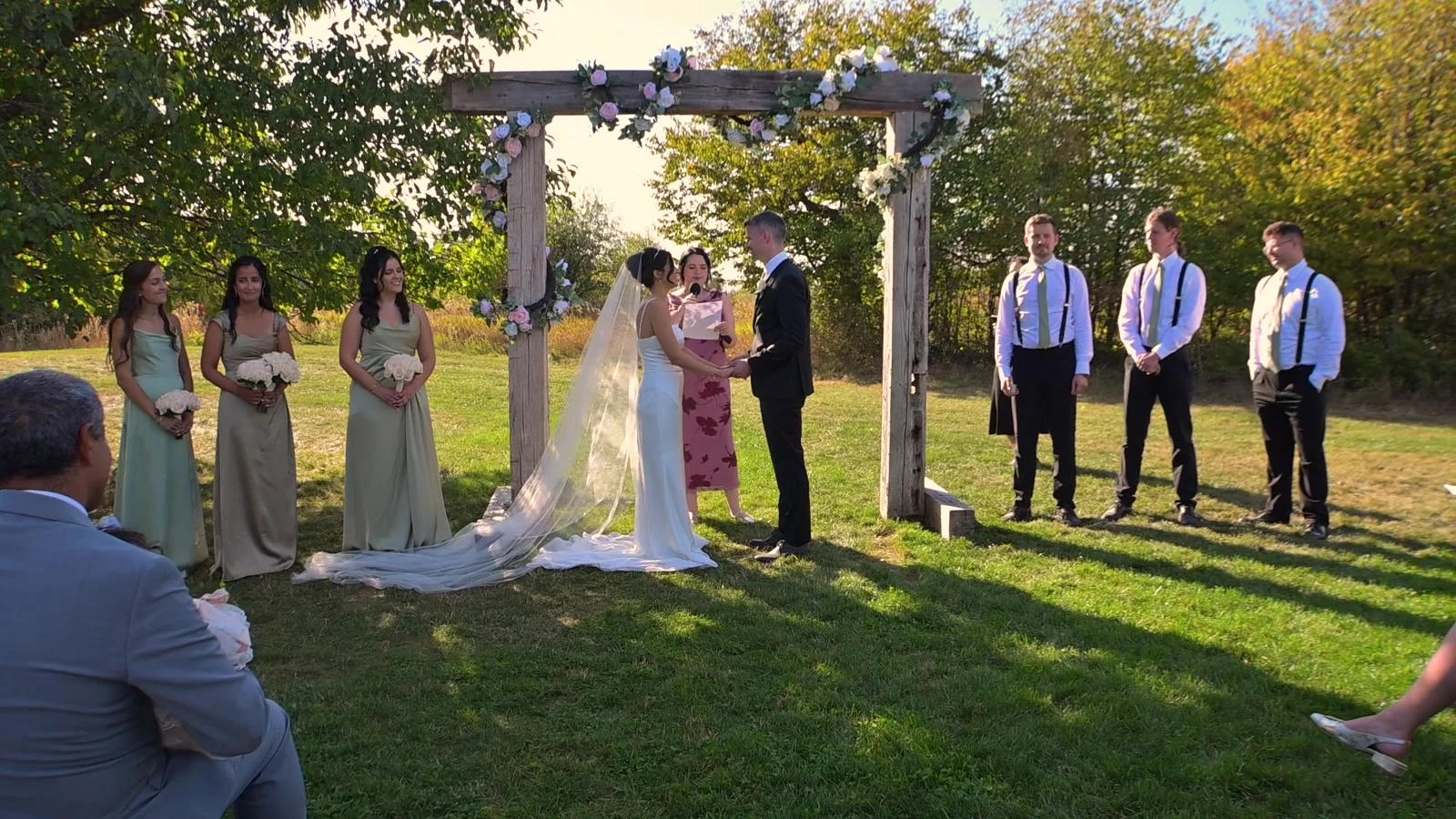 Kevin and Jodie beneath a floral ceremony arch, with attendants beside them